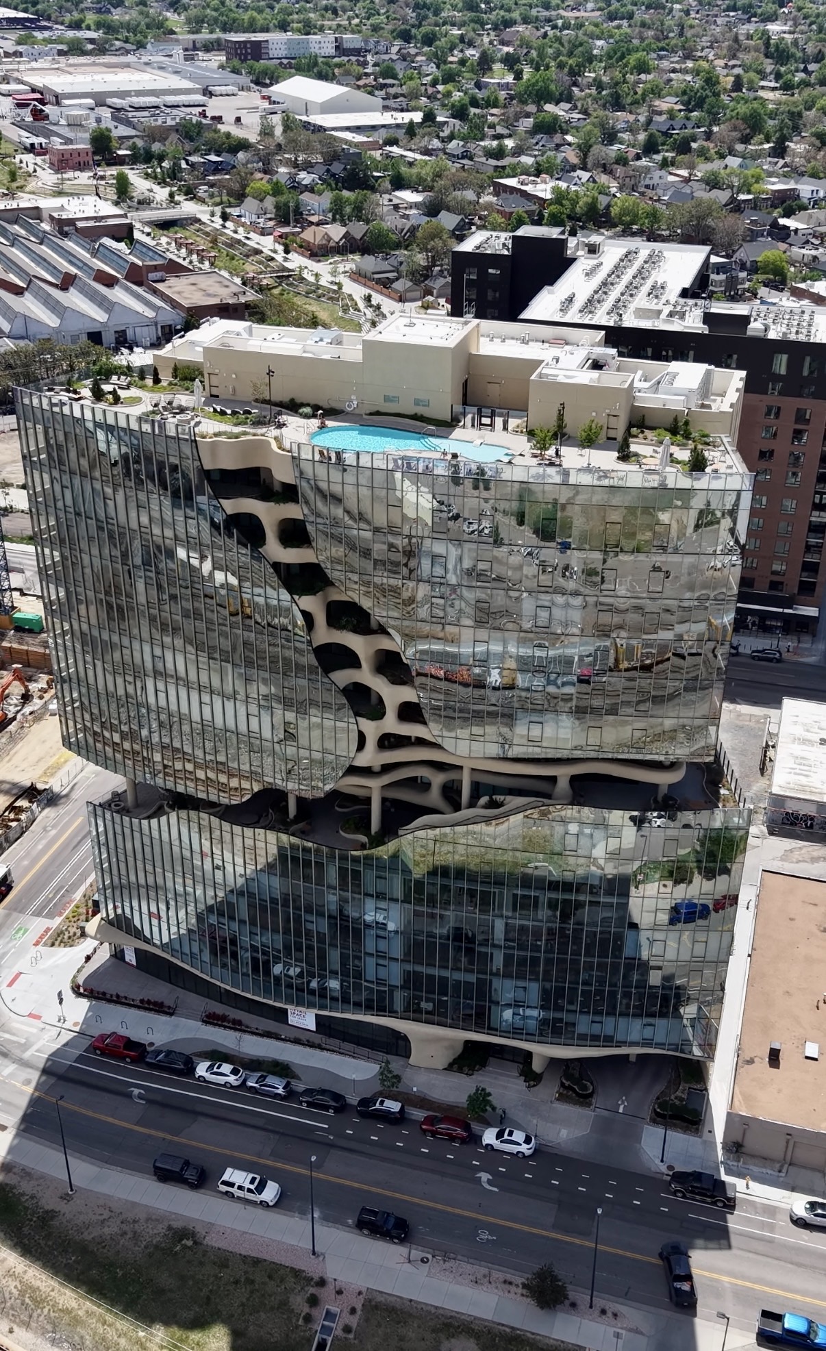 Aerial drone photograph of a modern glass apartment building with a rooftop pool deck and loungers